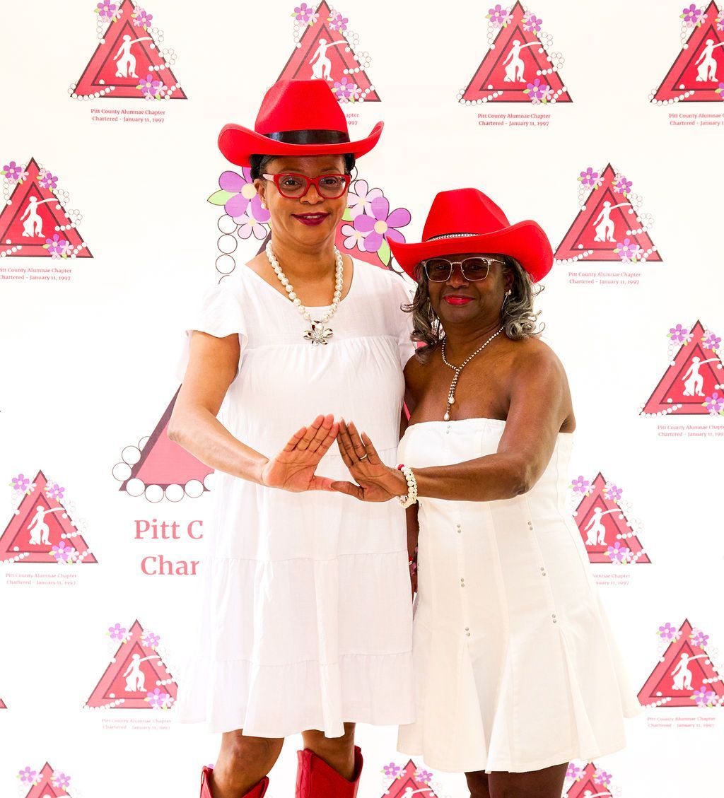 Two women in white dresses and red cowboy hats, posing, making a triangle with their hands.
