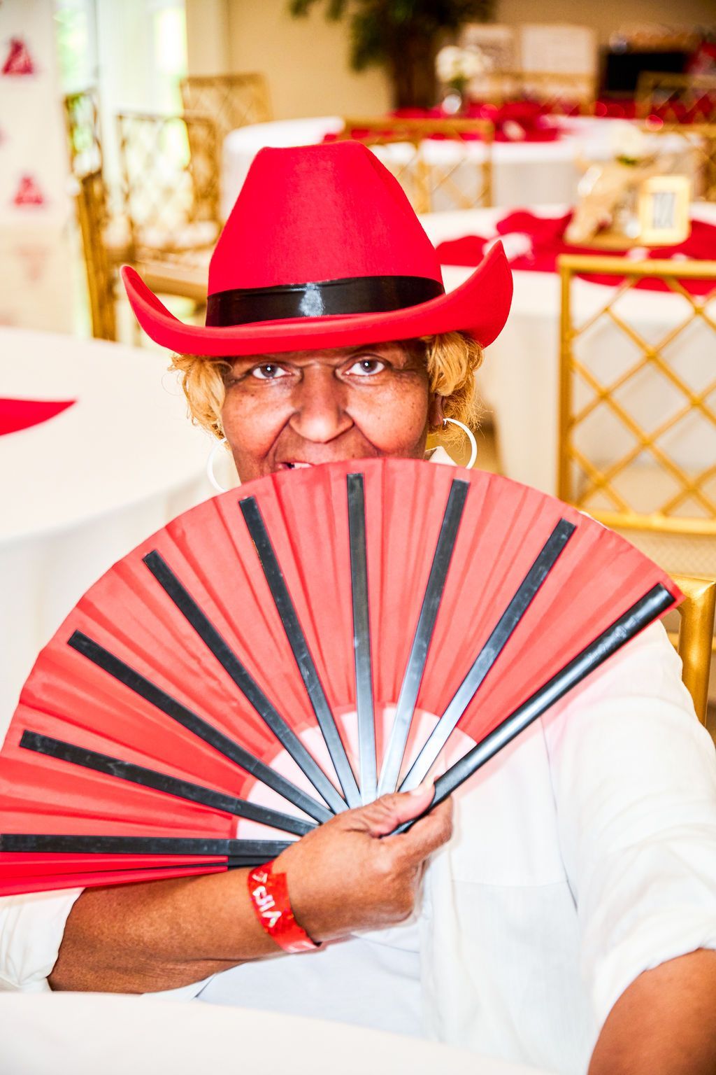 Person in red hat and fan at a table, smiling.
