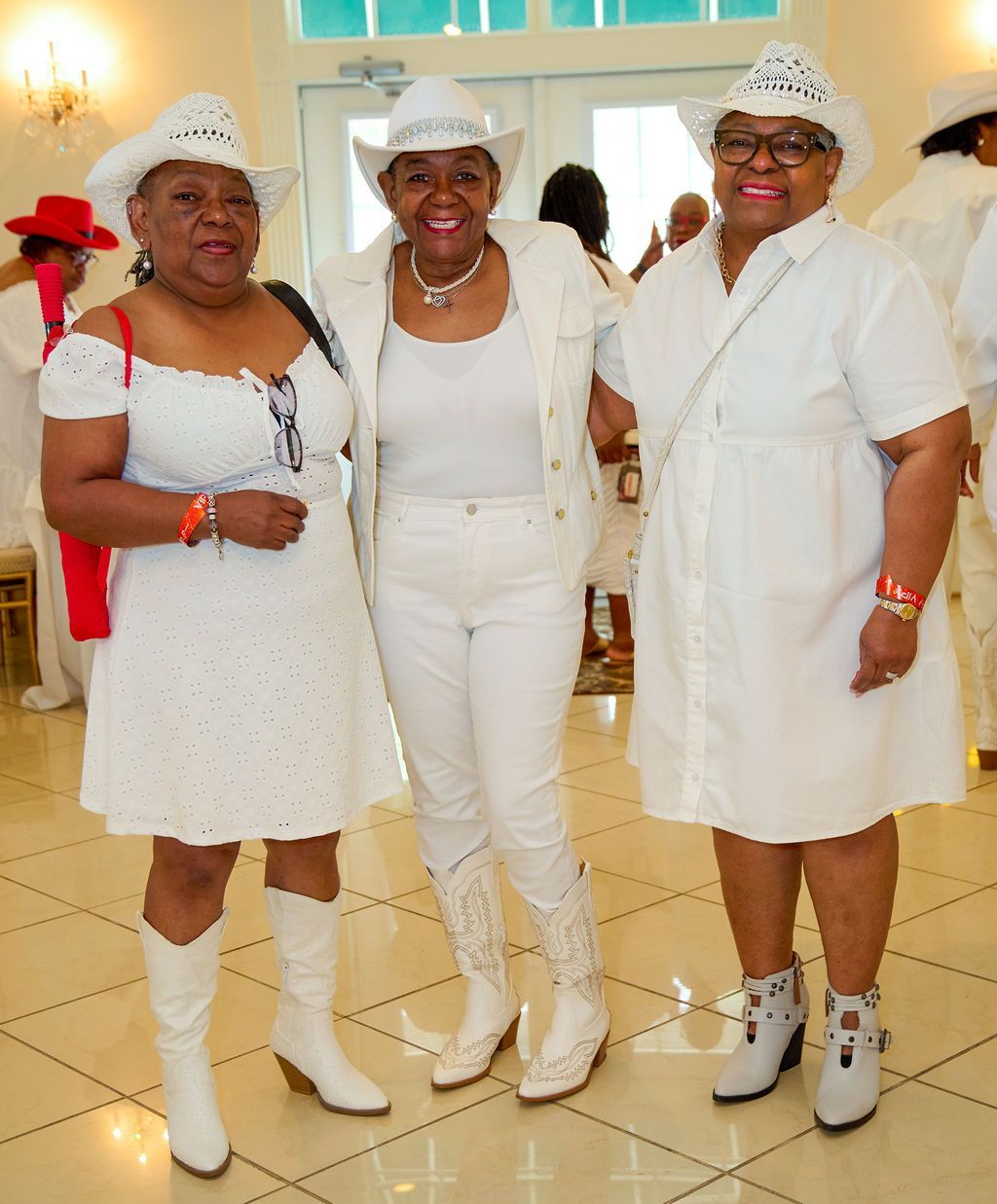 Three people in white outfits and cowboy hats smile indoors.
