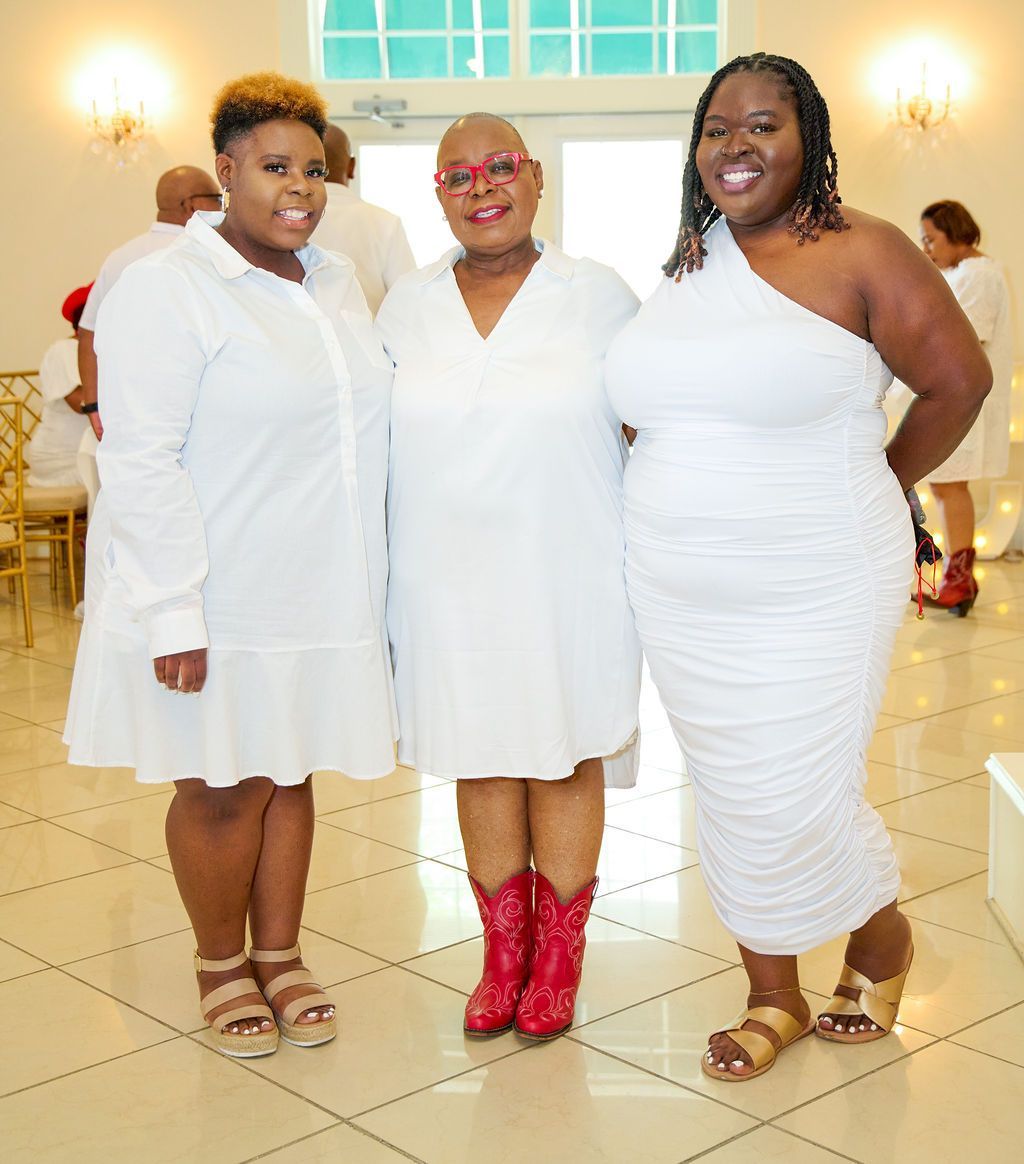 Three women in white outfits, two wearing sandals, one with red boots, posing indoors.