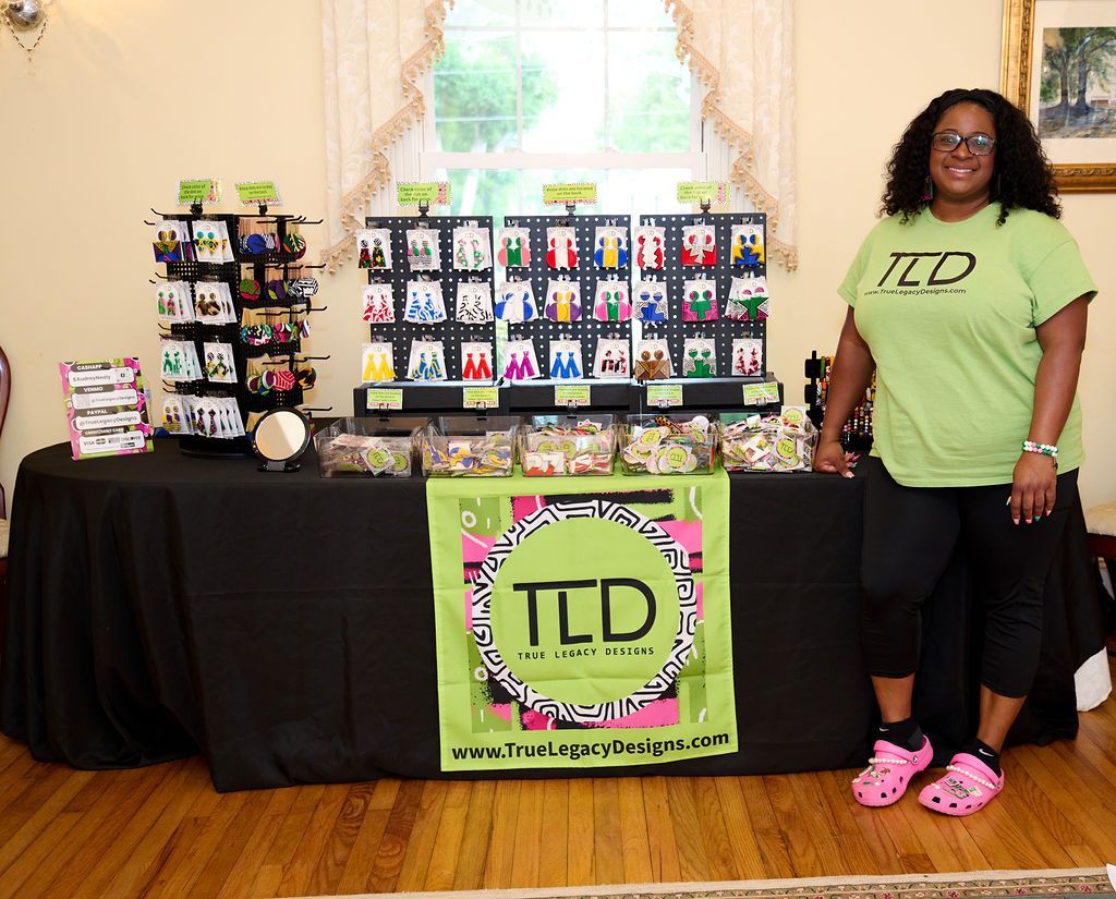 Woman at a table displaying colorful earrings, wearing a green T-shirt and pink Crocs.