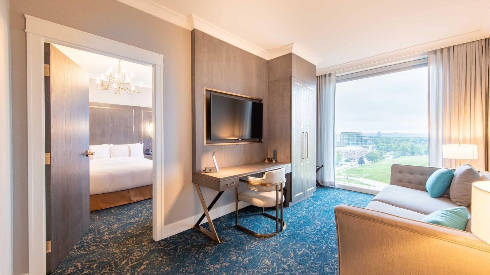 Hotel room interior with bed visible through doorway, desk, sofa, and large window.