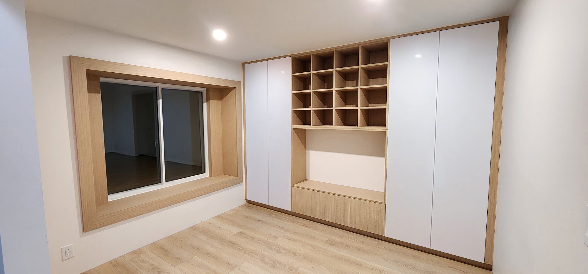 A room with a window and built-in wooden storage cabinets with white doors.