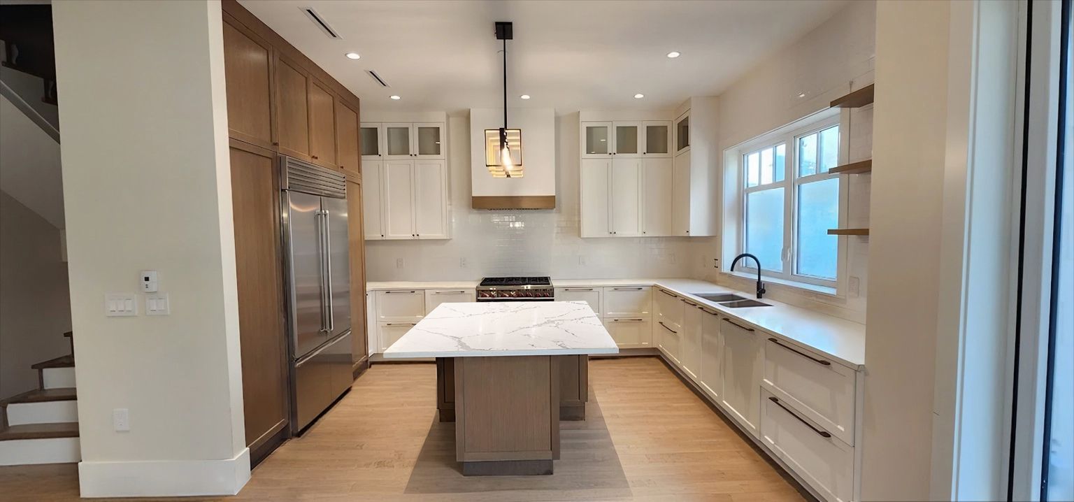 Modern kitchen with white and wood cabinets, a marble island, and stainless steel appliances.