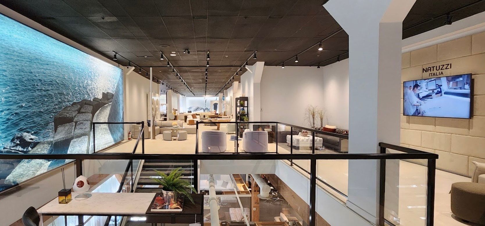 Interior view of a modern showroom with large wall display, staircase, and furniture.