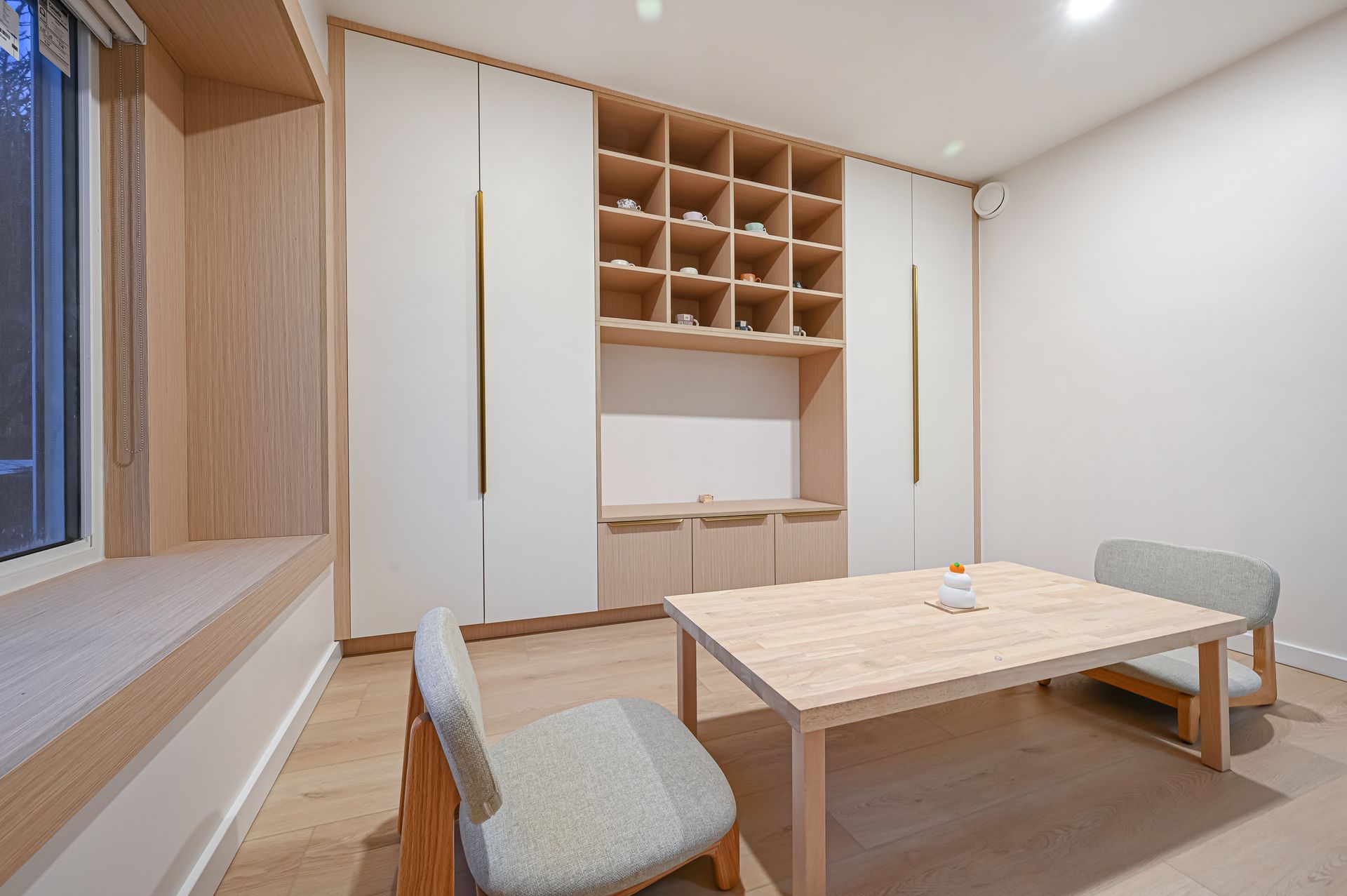 A light-wood dining area with a table, chairs, built-in shelving, and a window seat.