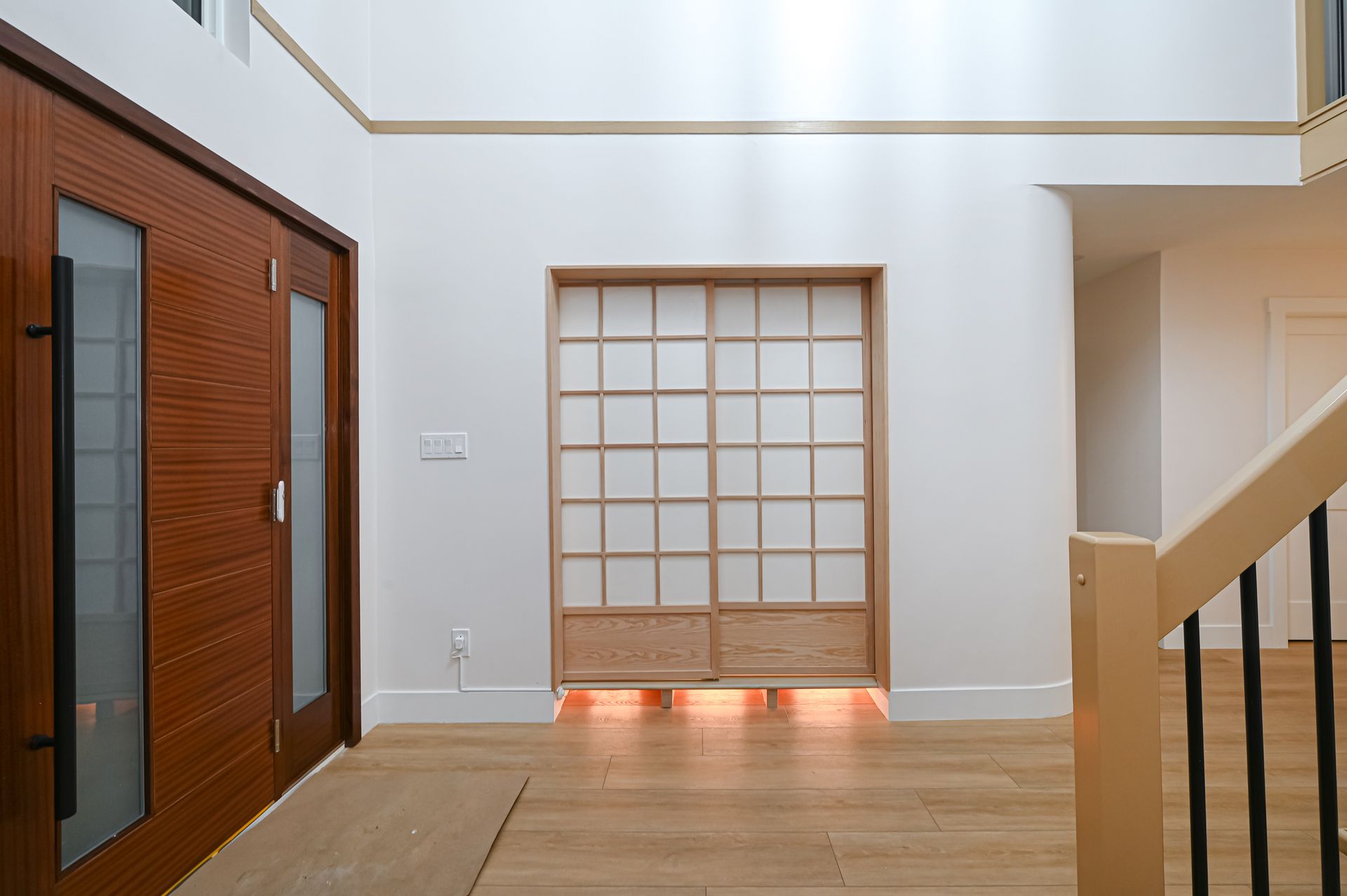 Wooden double doors, shoji screen, and staircase in a light-filled entryway.