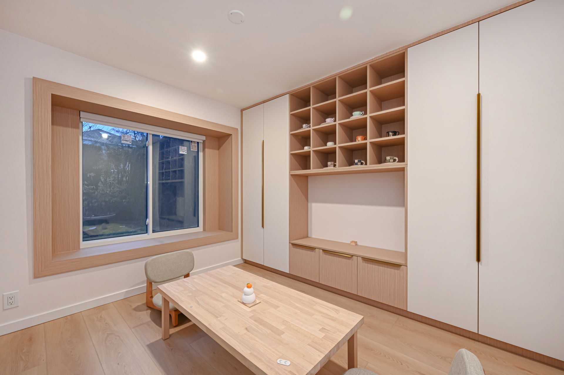 Interior of a room with light wood furniture, white cabinetry, and a window.