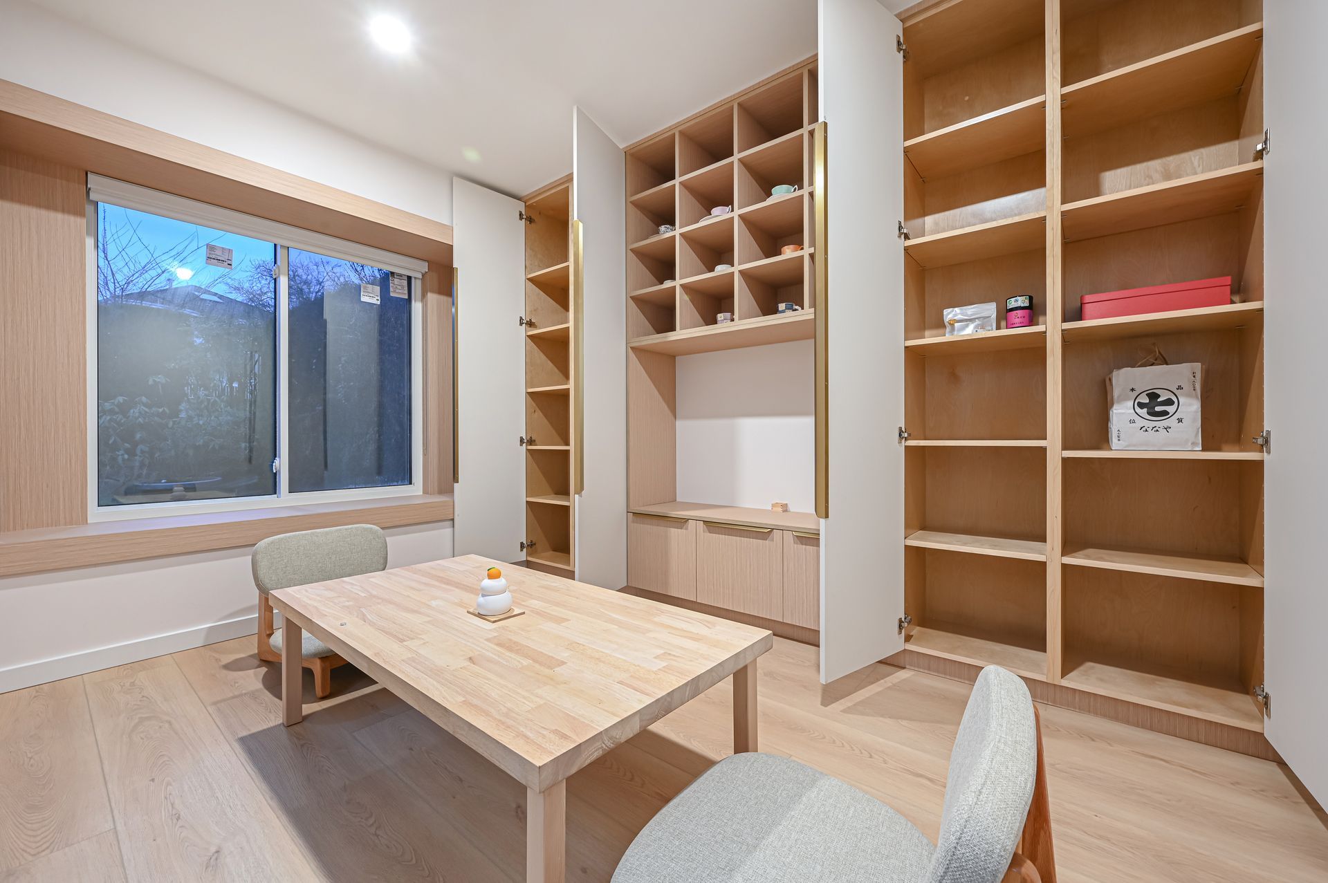 Room with wooden shelves, table, chairs, and a window; light wood and neutral tones.