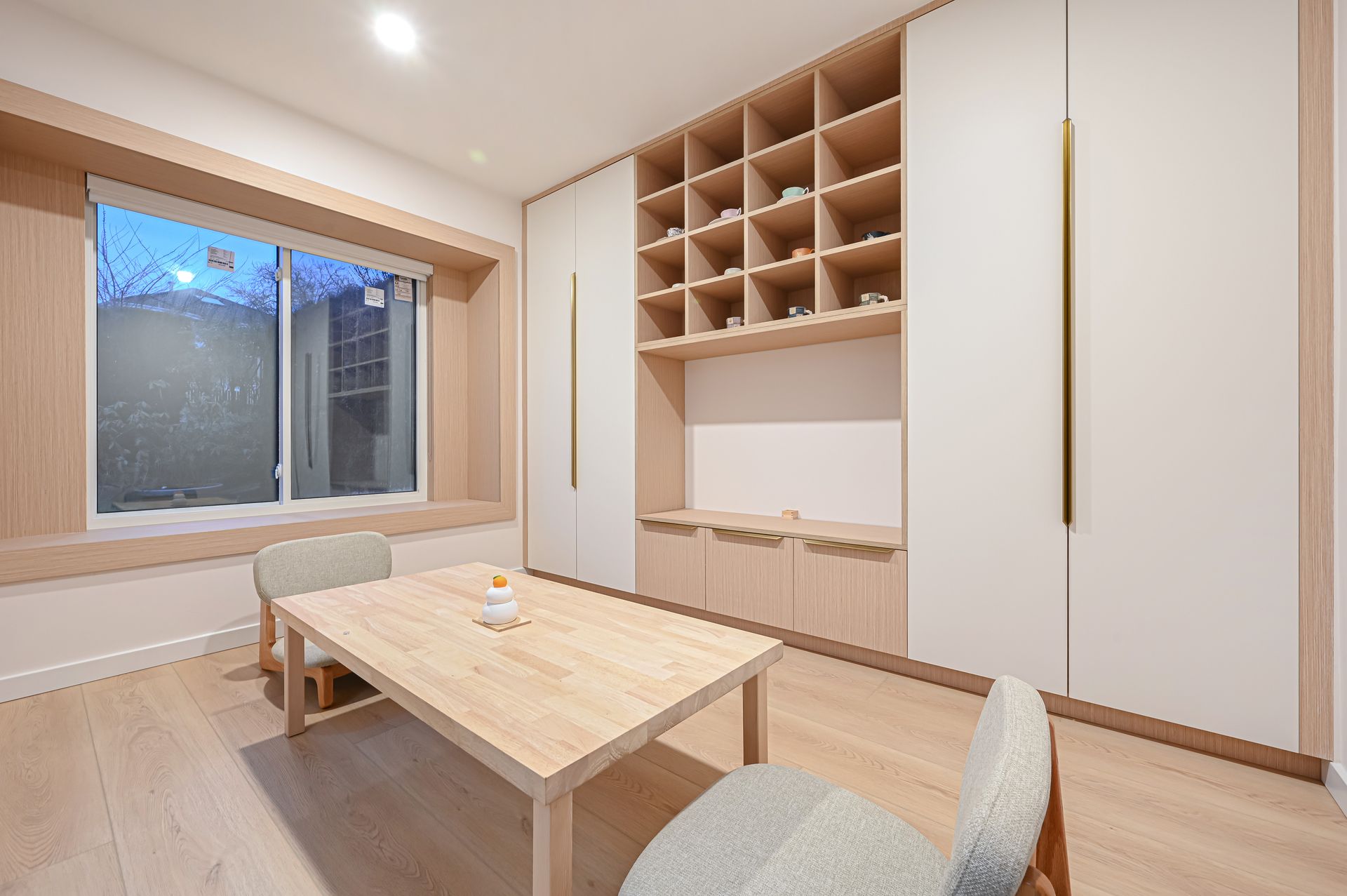 A light-filled room with a wooden table and chairs, built-in shelving, and a window.