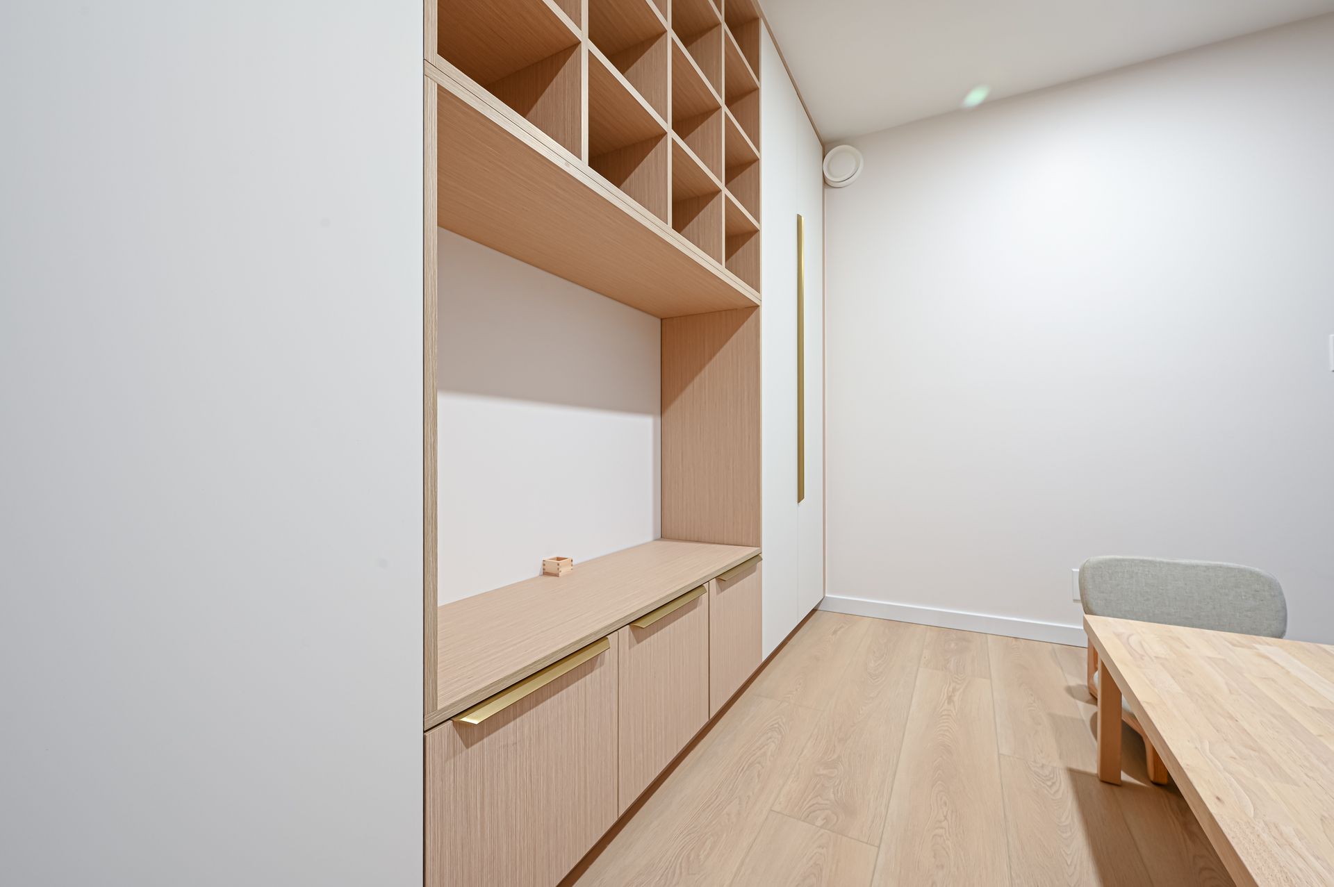 Built-in wooden shelving unit with cabinets, cubbies, and a desk in a room with light wooden floors and white walls.