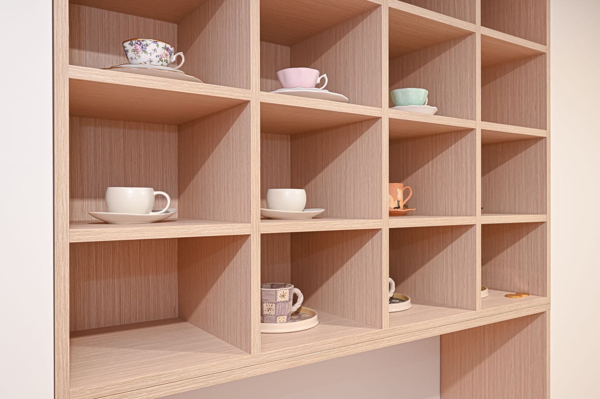 Wooden cubby shelf with teacups and saucers displayed in the compartments.