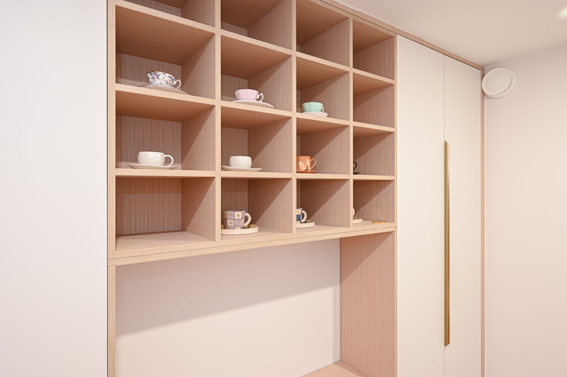 Wooden cubby shelves holding teacups and saucers built into a light-colored wall.