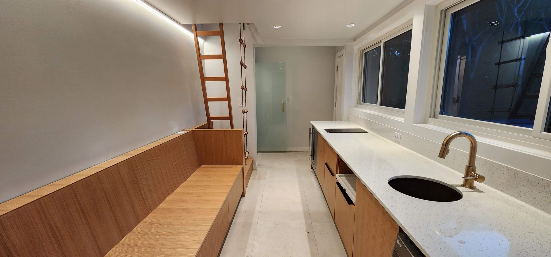 A small, modern kitchen with light wood cabinets, white countertops, and a built-in bench.