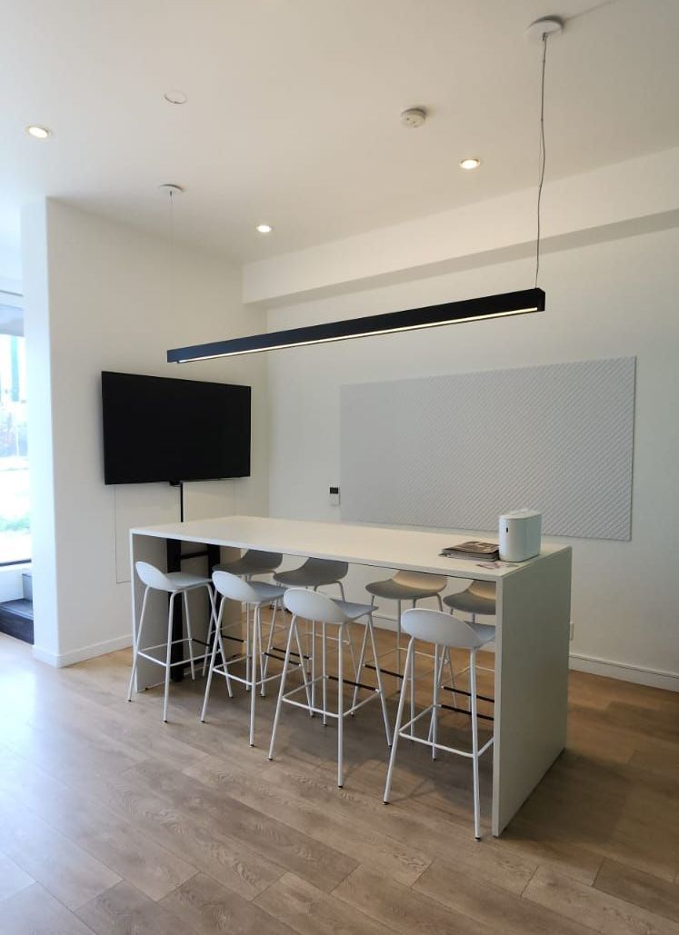 A modern kitchen island with bar stools, TV, and long light fixture. White walls and wood floor.