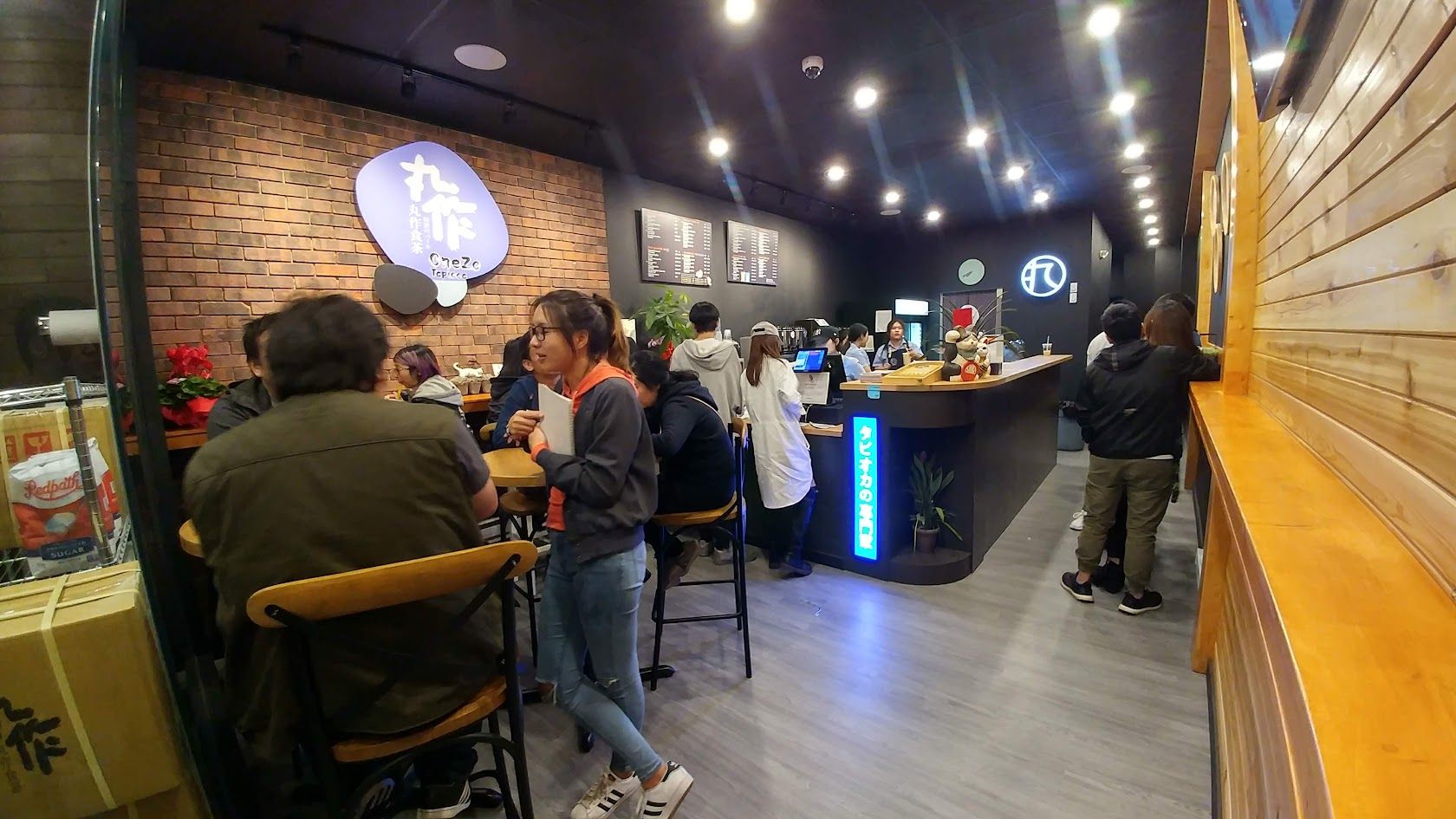 Interior of a crowded tea shop with customers seated at tables and standing at a bar.