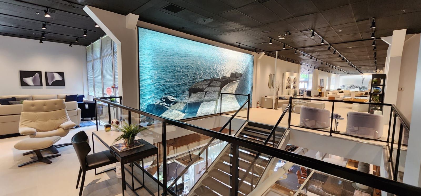 Interior of a furniture store with a large wall mural of a seascape. A staircase leads to a second level.