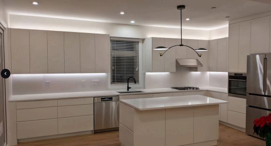 Modern kitchen with white cabinetry, stainless steel appliances, and island with overhead lighting.
