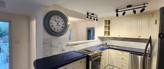 Kitchen with blue countertops, cream cabinets, and large clock.