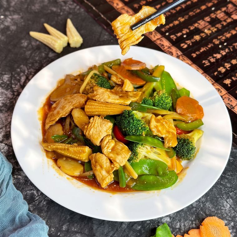 Plate of chicken and vegetables in brown sauce, with broccoli, carrots, and baby corn on a table