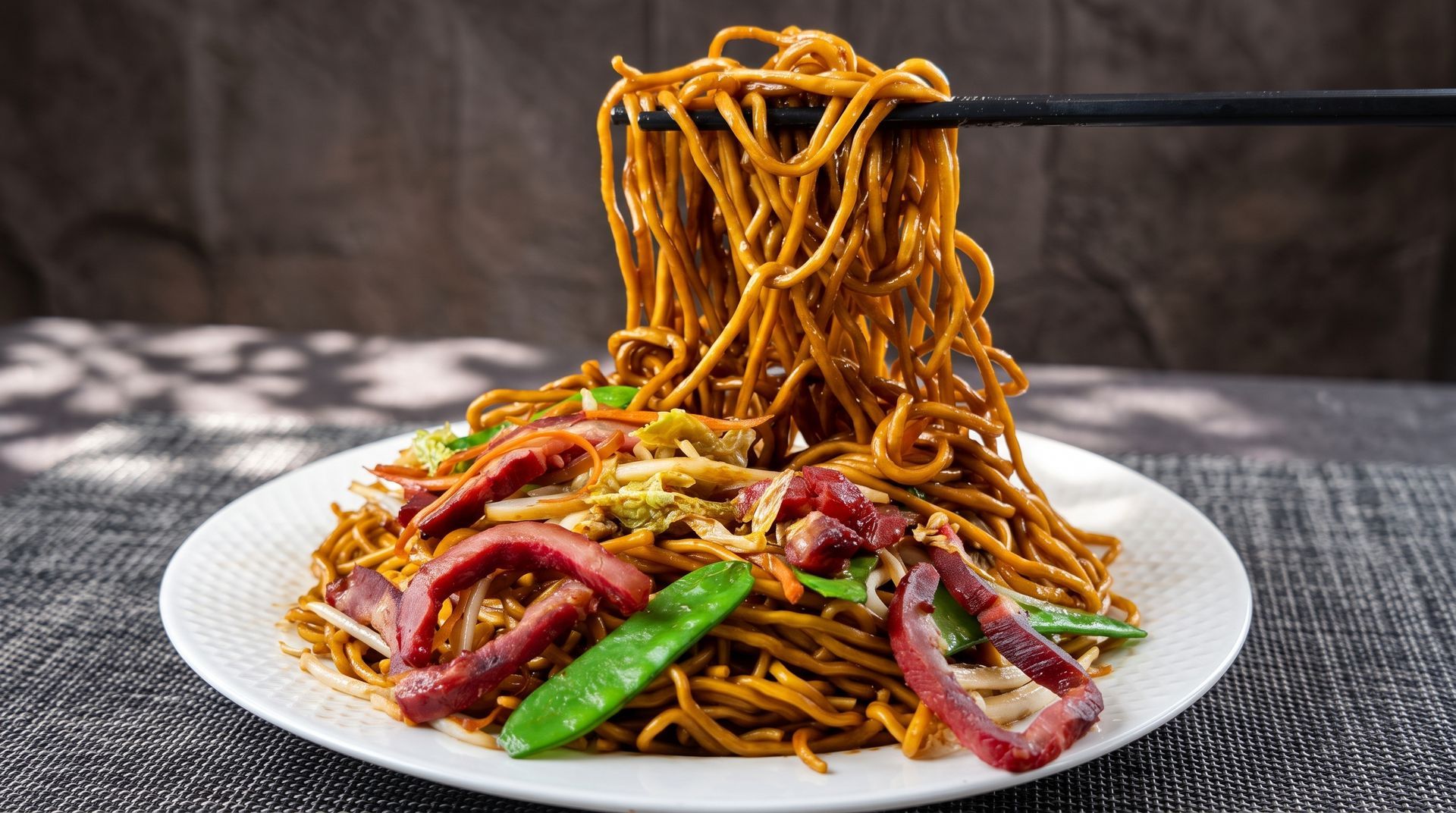 Plate of stir-fried noodles with sliced meat and green peppers, garnished with herbs, on a dark table