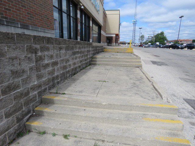 Exterior steps and sidewalk along a brick building but no guardrail for safety