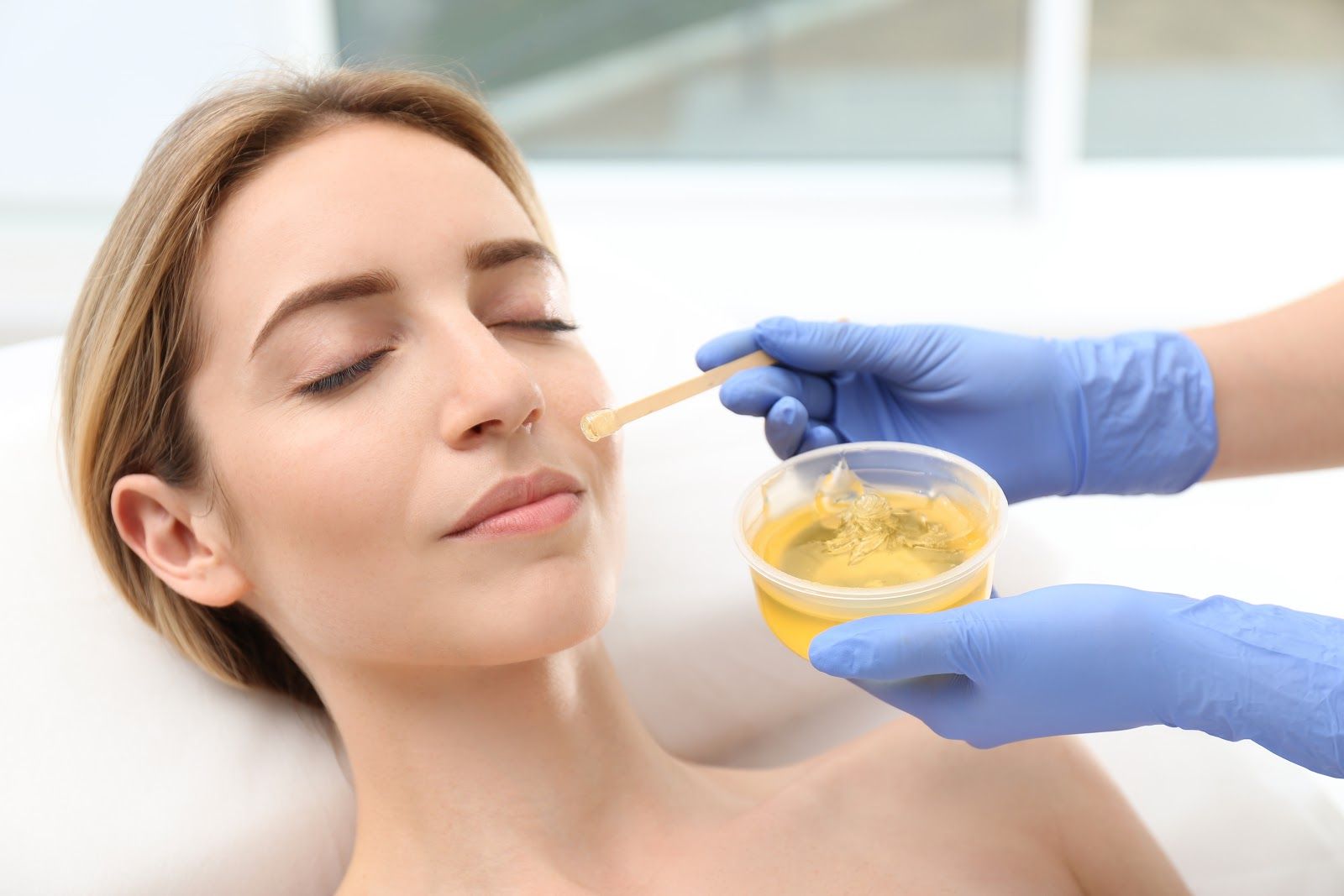 Gloved hands apply yellow facial mask to a woman’s nose in a spa treatment