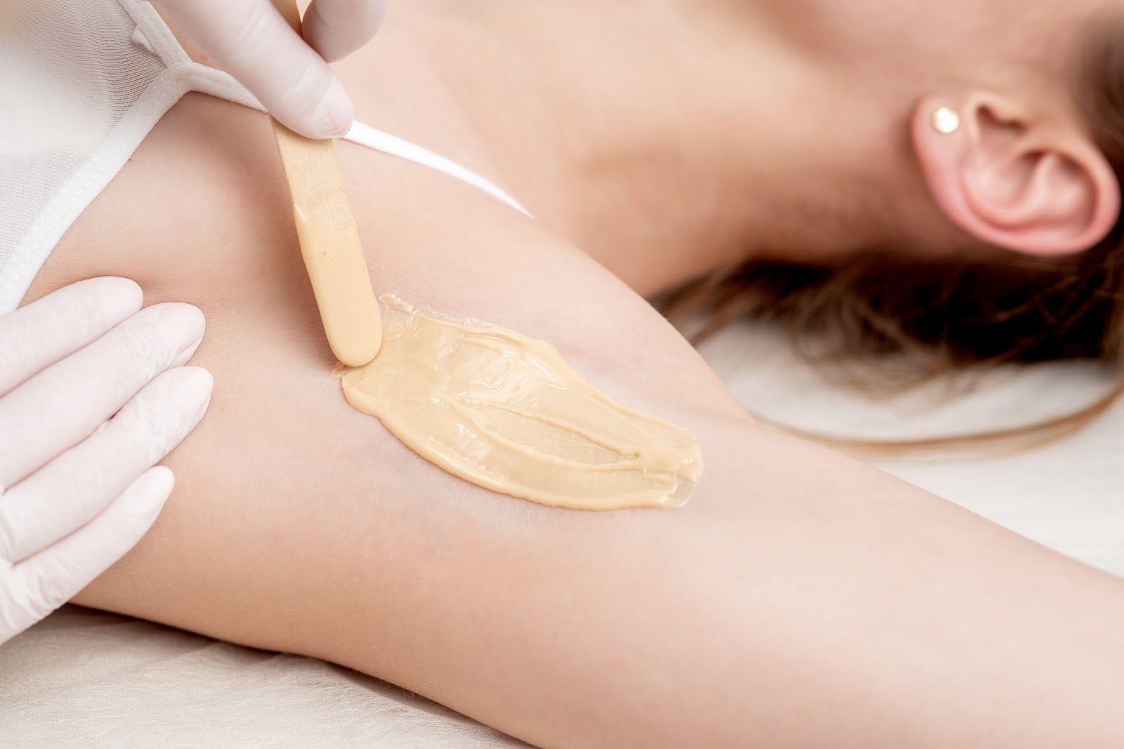 Wax being applied to an underarm with a wooden spatula and gloved hands