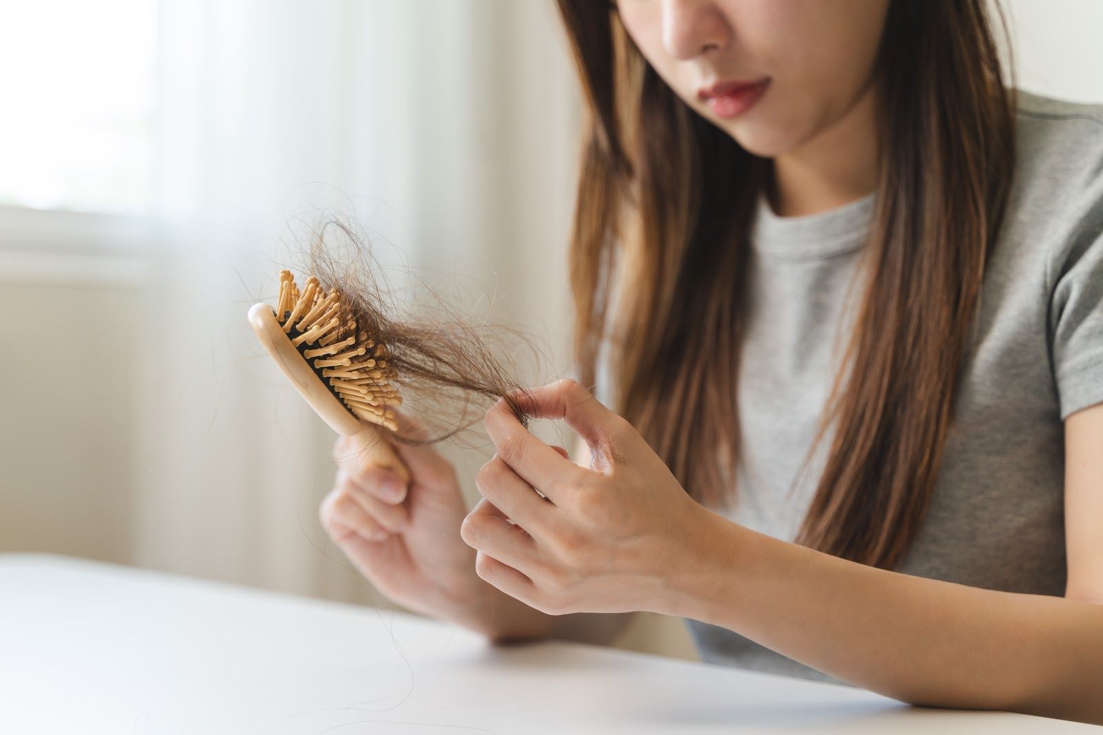 Woman brushing a wooden hairbrush with tangled hair strands on a white table