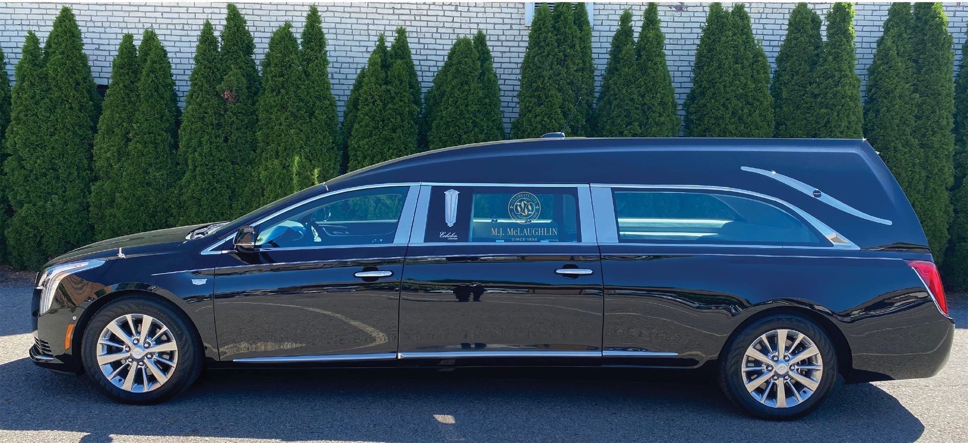a black funeral car is parked in front of a brick building with trees in the background .