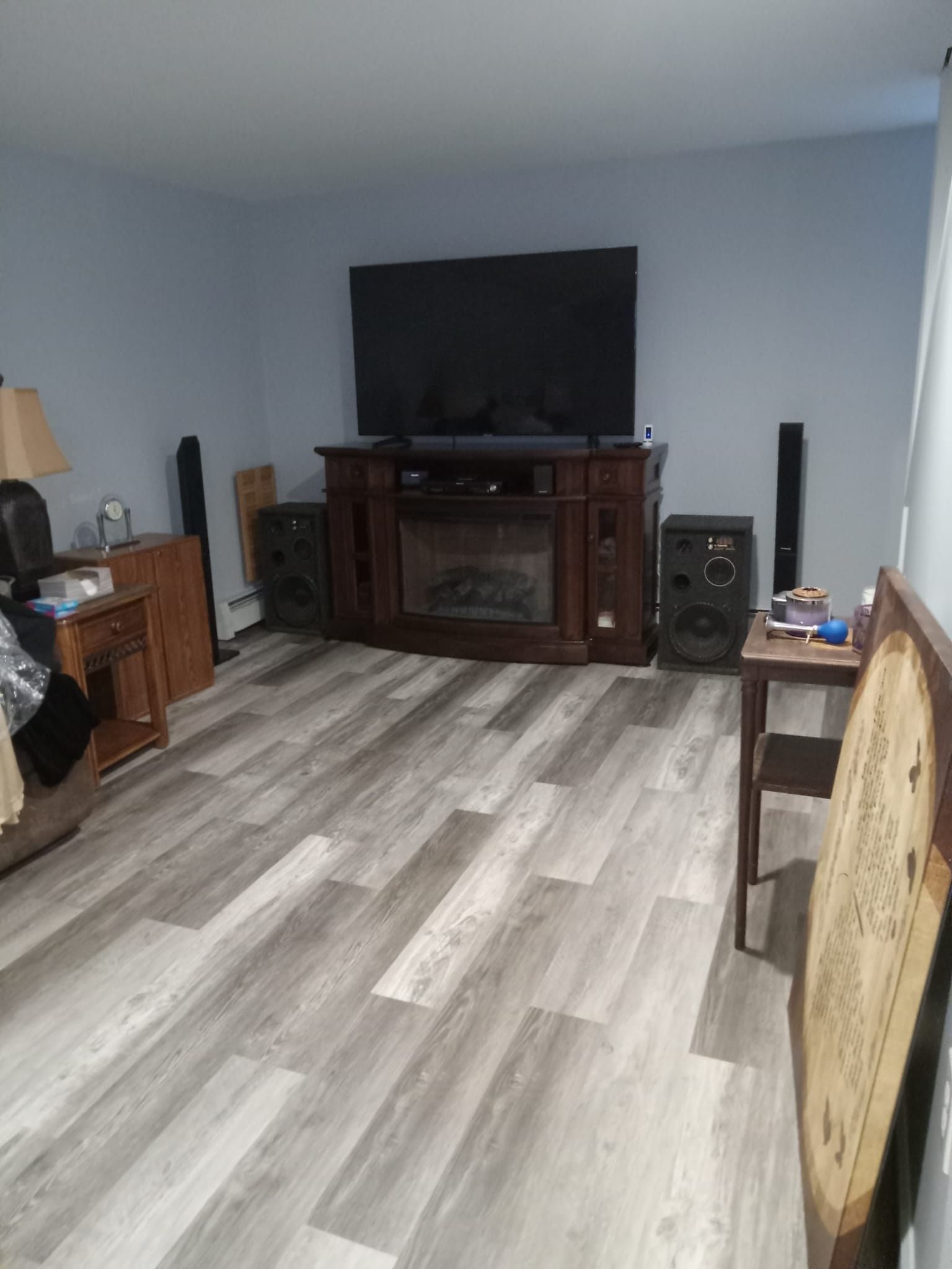 Empty living room with gray flooring, large TV, and dark wooden entertainment center.