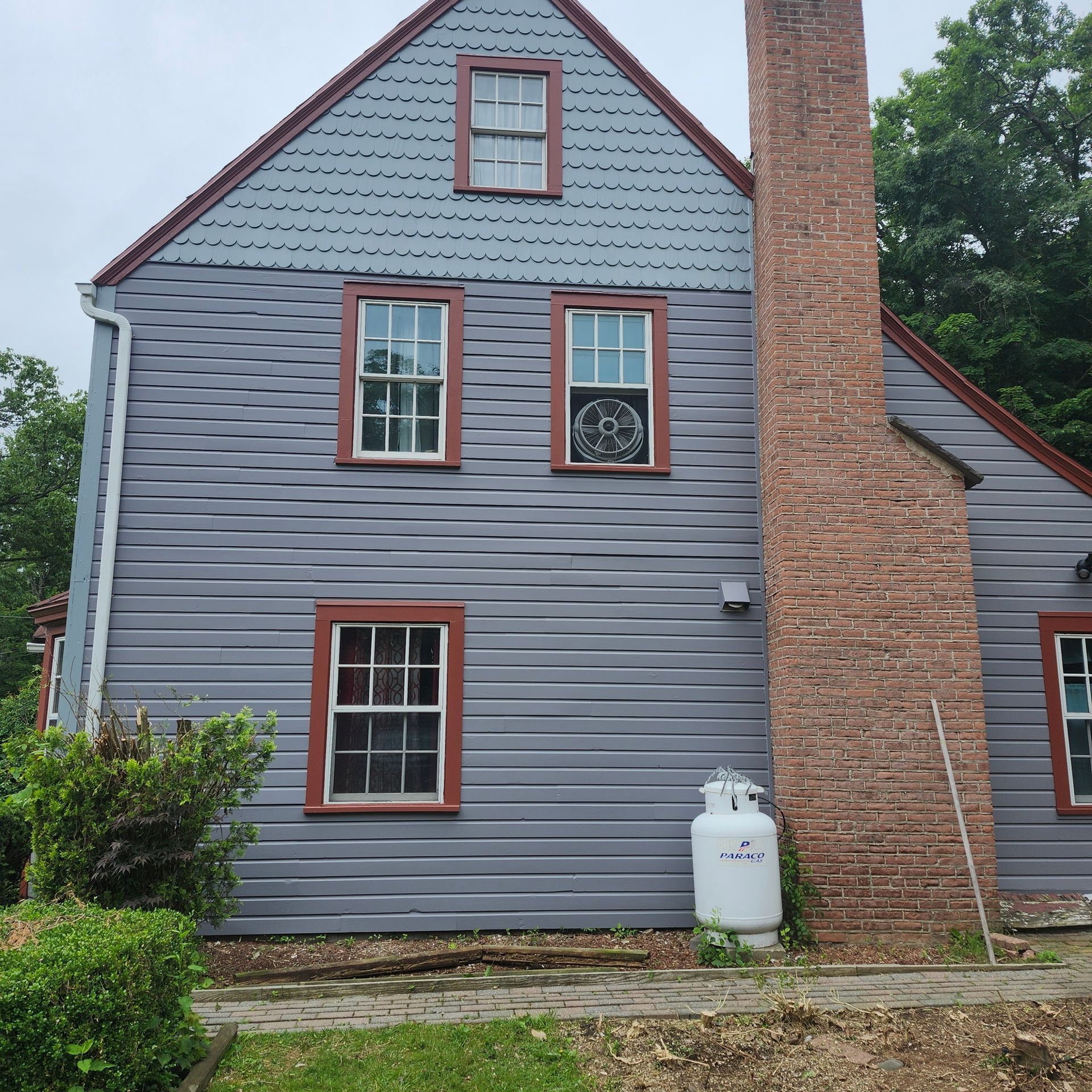 Gray house with red-trimmed windows and a brick chimney, viewed from the side.