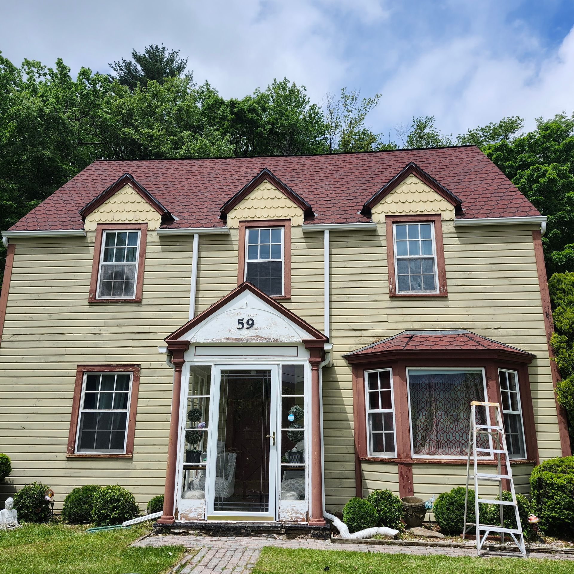 Two-story beige house with red roof and front porch, number 59, ladder leaning against right side