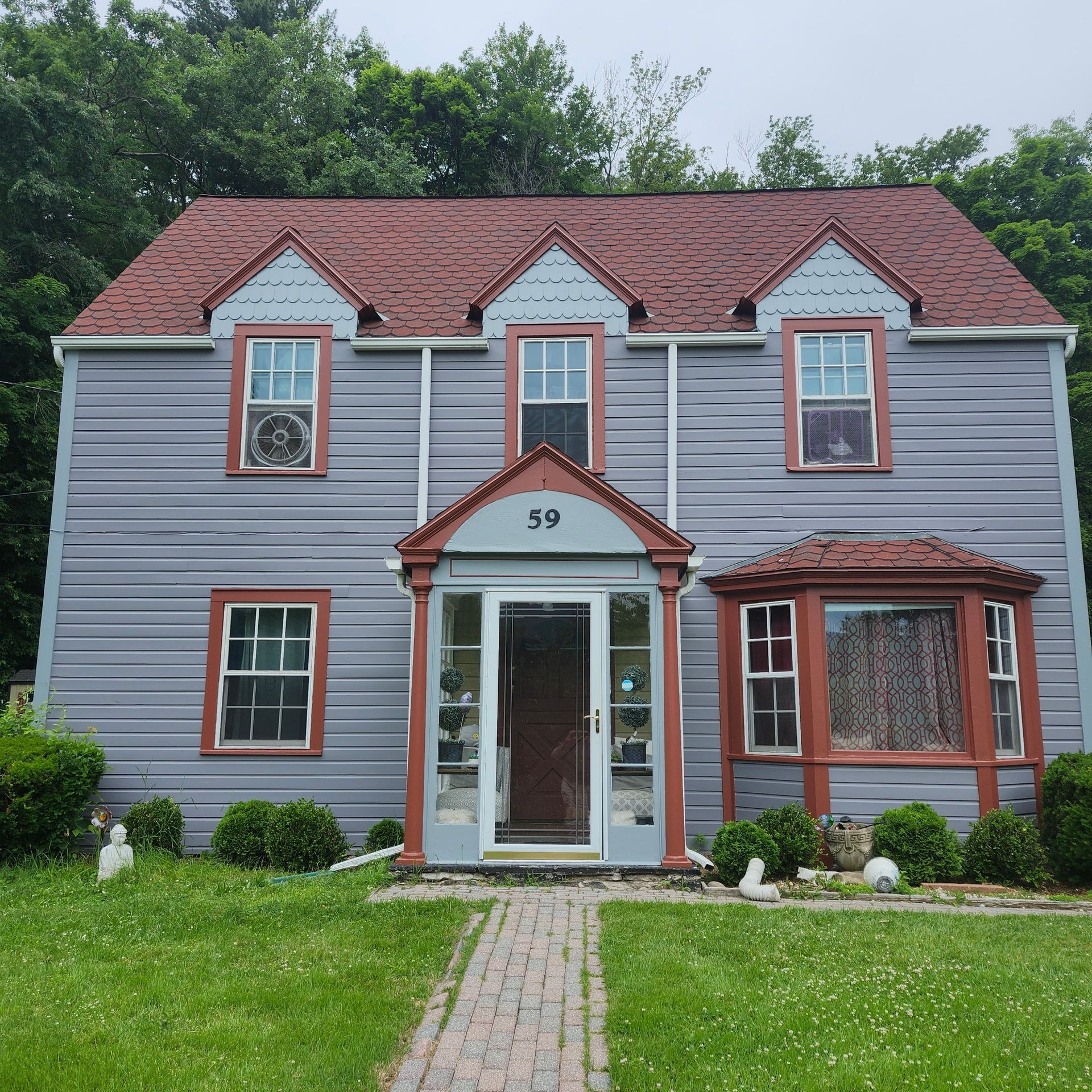 Gray two-story house with red roof and white trim, front walkway, and green lawn