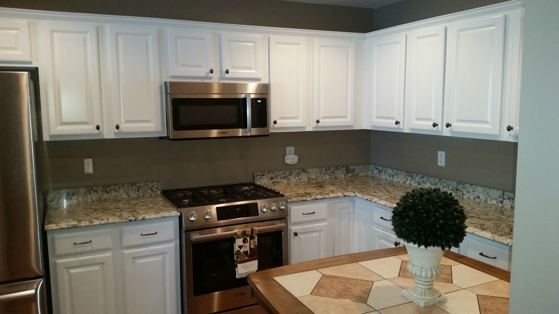 Bright white kitchen with granite counters, stainless appliances, and a small table in the foreground