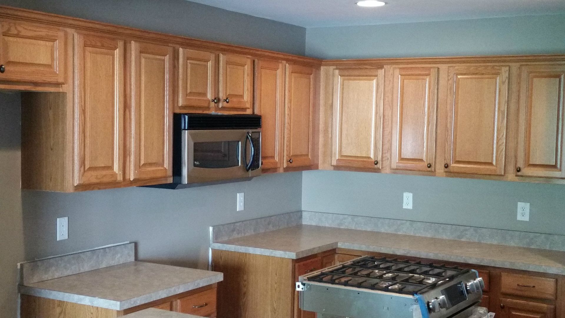 Kitchen with light wood cabinets, gray walls, stainless microwave, and a gas stove beneath a tiled backsplash.