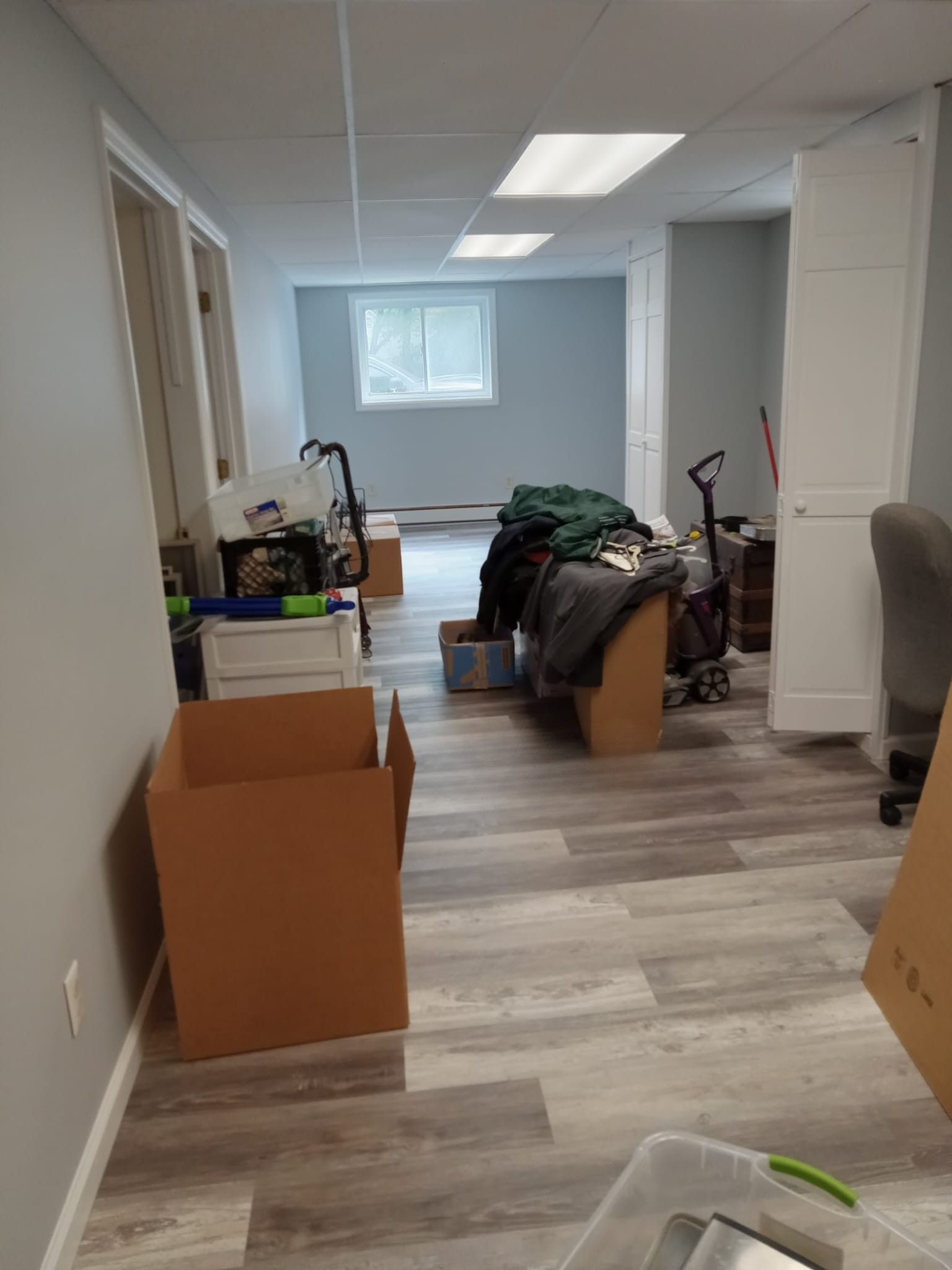 Cluttered room with moving boxes, stacked items, and a small window at the back.