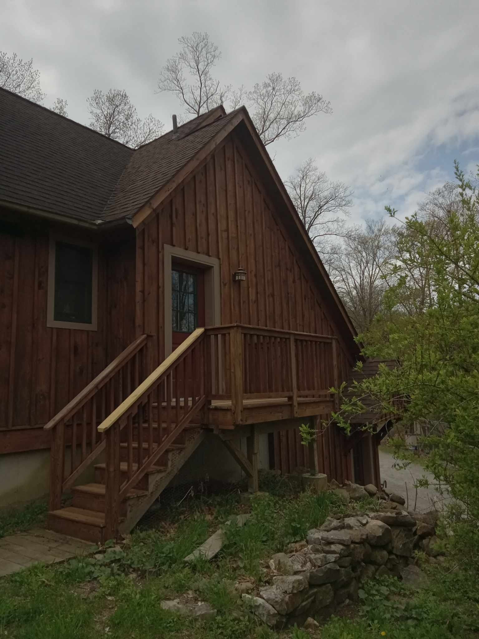Wooden cabin with steep roof and small porch beside a rocky stream under overcast sky