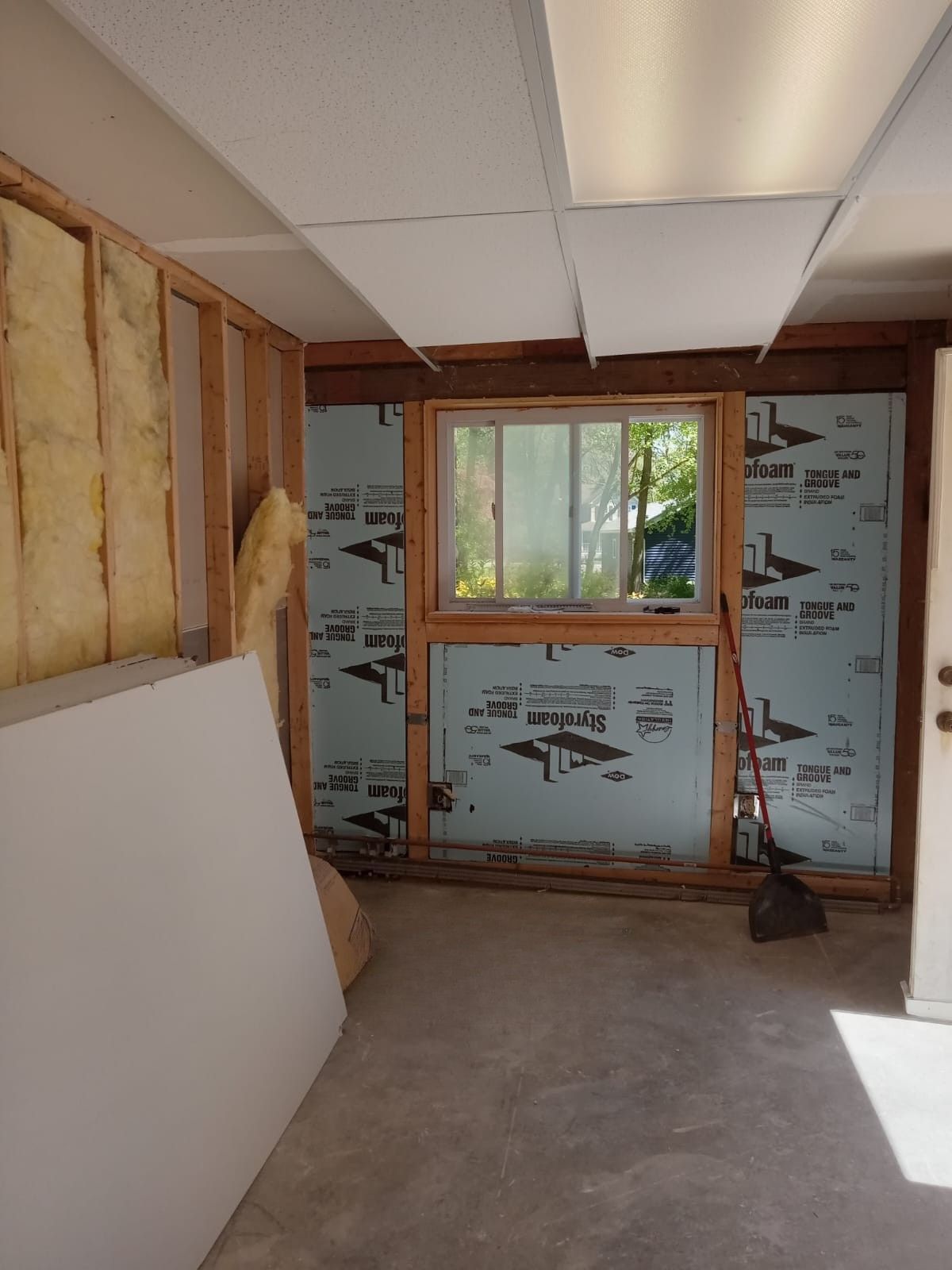 Partially renovated room with exposed insulation, a window, and drywall leaning against the wall