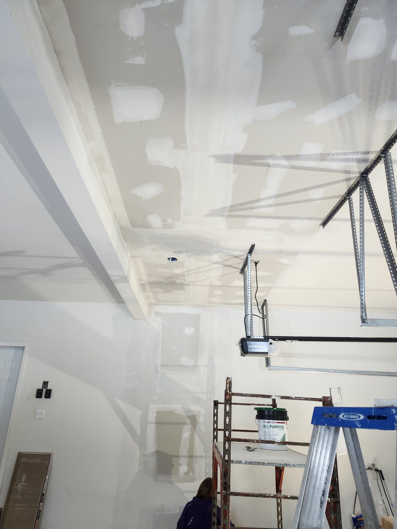 Partially finished room with drywall ceiling patches, scaffolding, and a step ladder under construction light fixtures