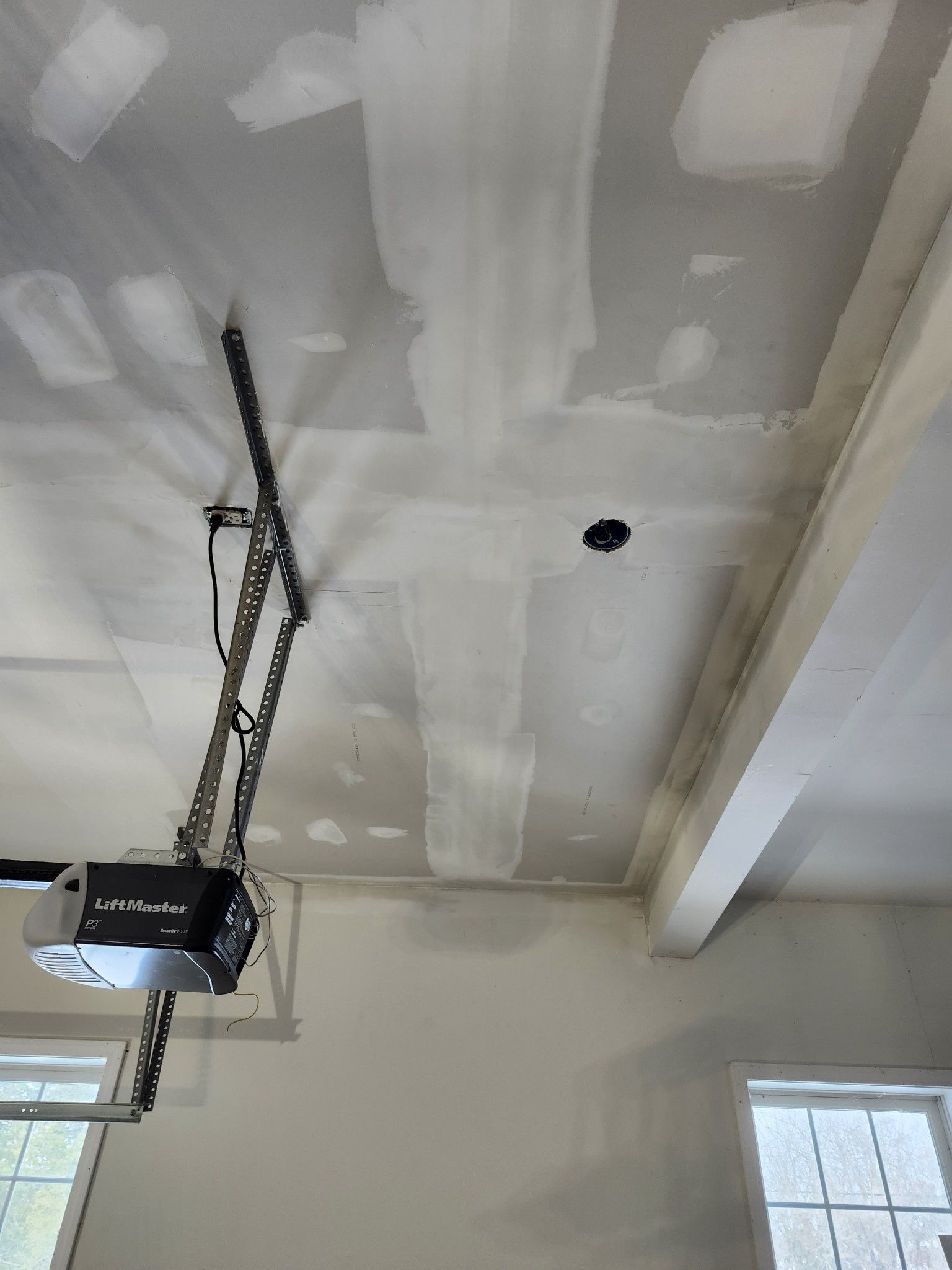 Garage ceiling with drywall patches, a hanging opener, and windows along the wall