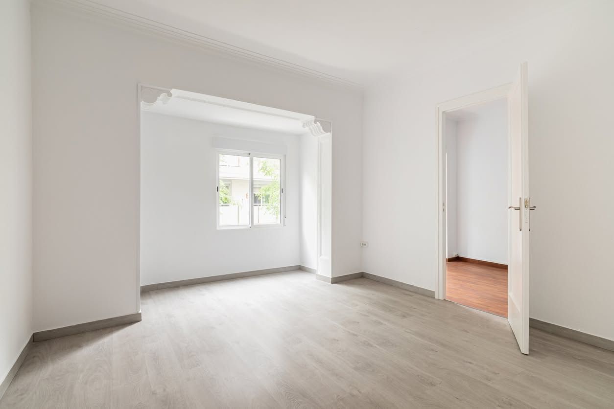 Empty white room with light wood floors and a doorway to a second room with a window