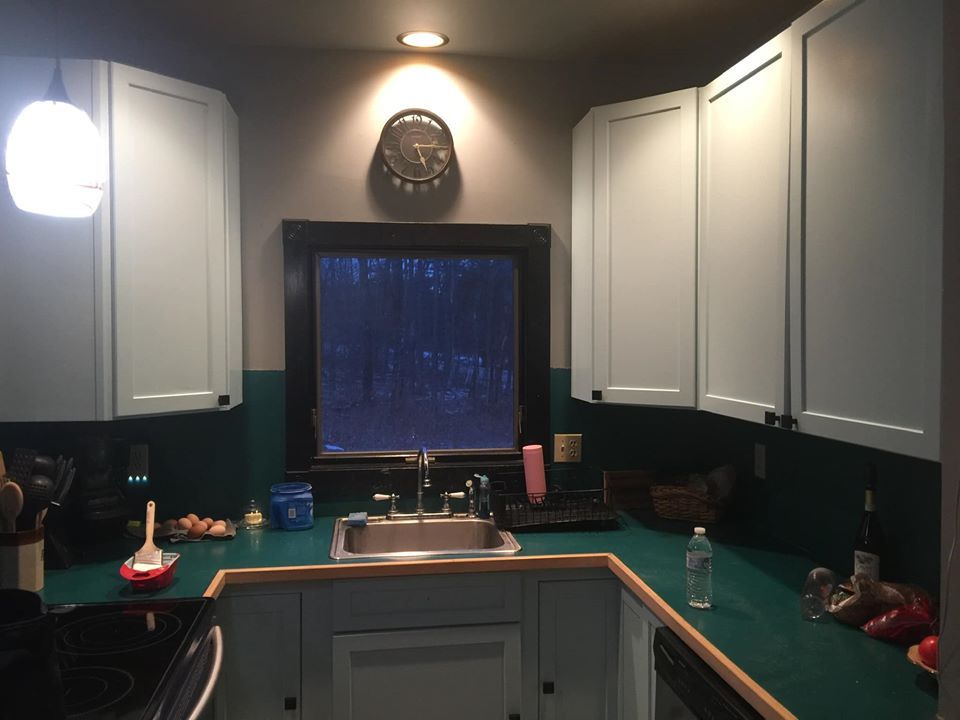 Kitchen with white cabinets, dark green backsplash, and a window over the sink at night.