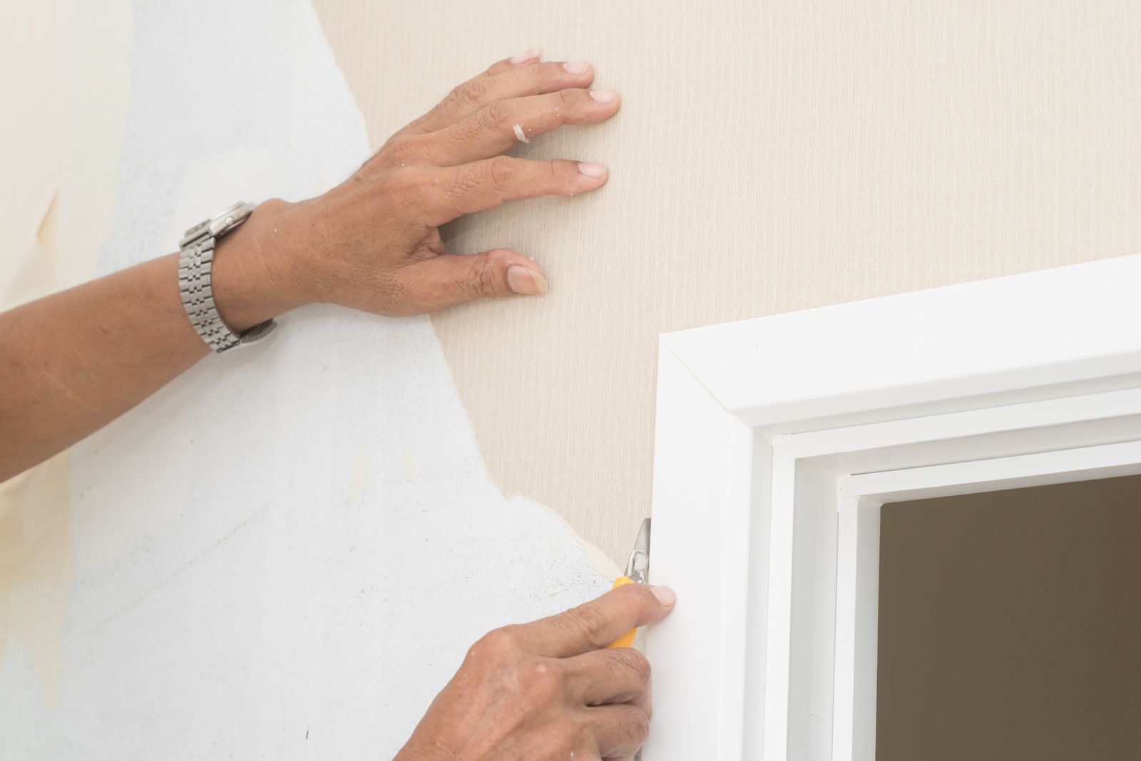 Hands painting beige wall edges around a white door frame with a small brush.