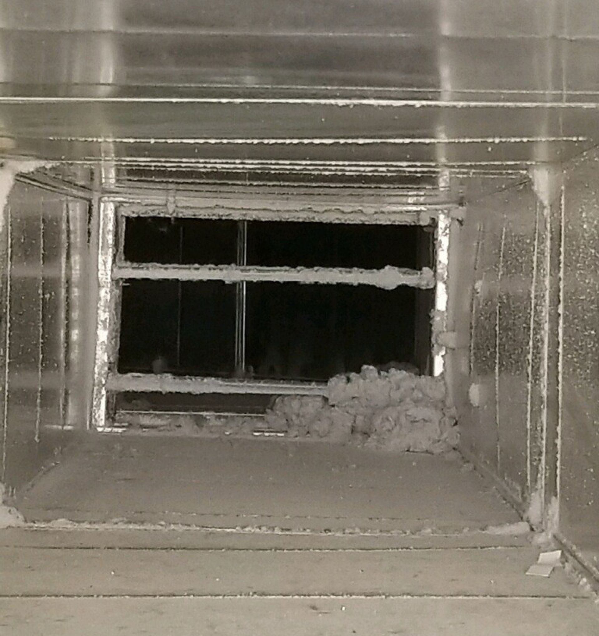 Dusty vent opening with horizontal slats and debris buildup inside a narrow duct.