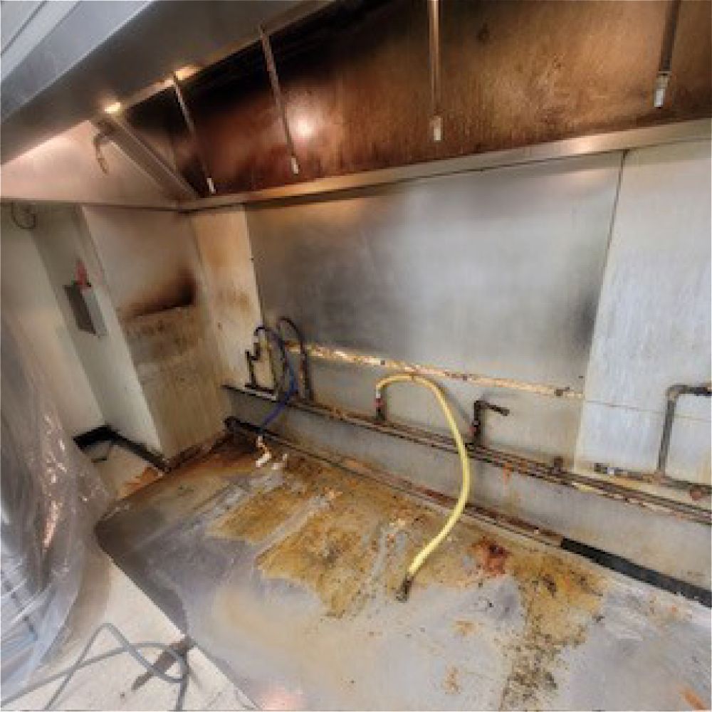 Damaged commercial kitchen wall with heavy smoke stains, exposed pipes, and a dirty floor.