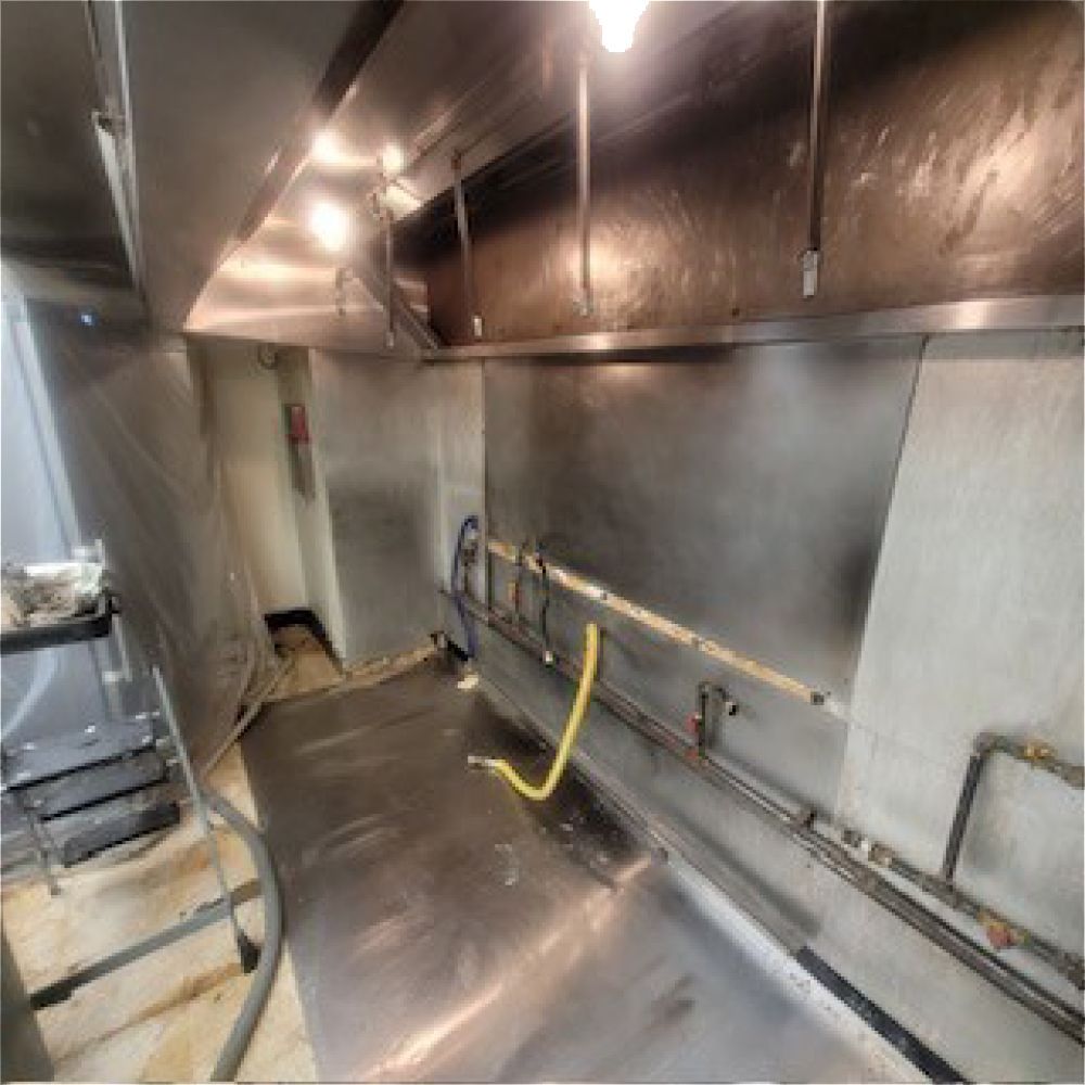 Empty, dirty, rectangular cargo trailer interior; light at the far end; white walls, soiled floor. Stainless steel kitchen, vent hood, work surface, and piping.