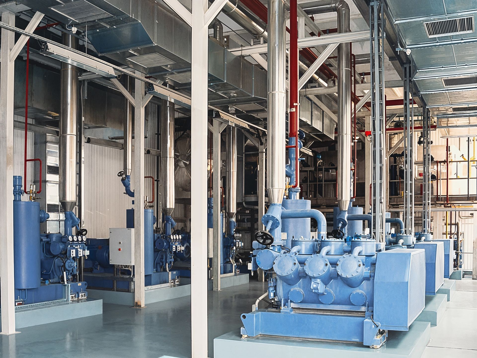 Carpet being cleaned with a professional cleaning tool, showing white and gray diamond pattern. Blue industrial refrigeration equipment inside a clean building with pipes and supports.
