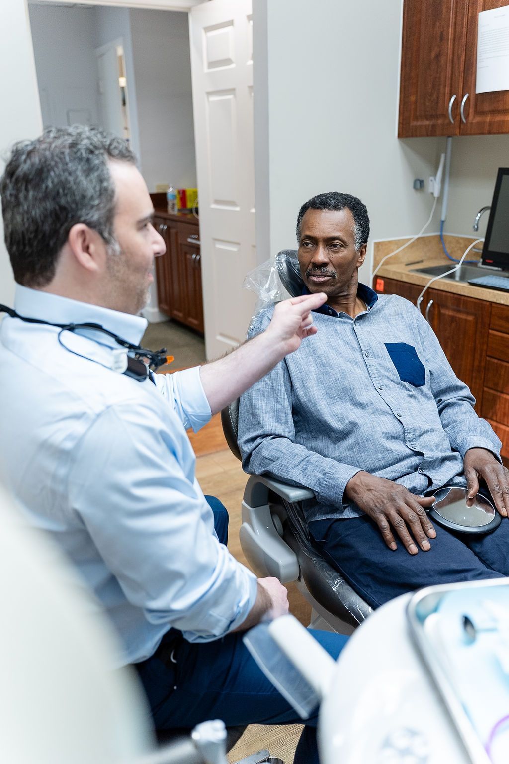 Doctor examining a seated patient in a clinic exam room.