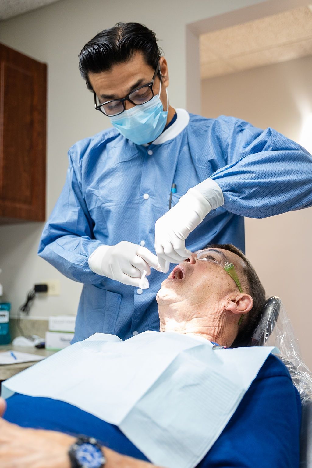Dentist in blue protective gear treating a patient in a dental chair